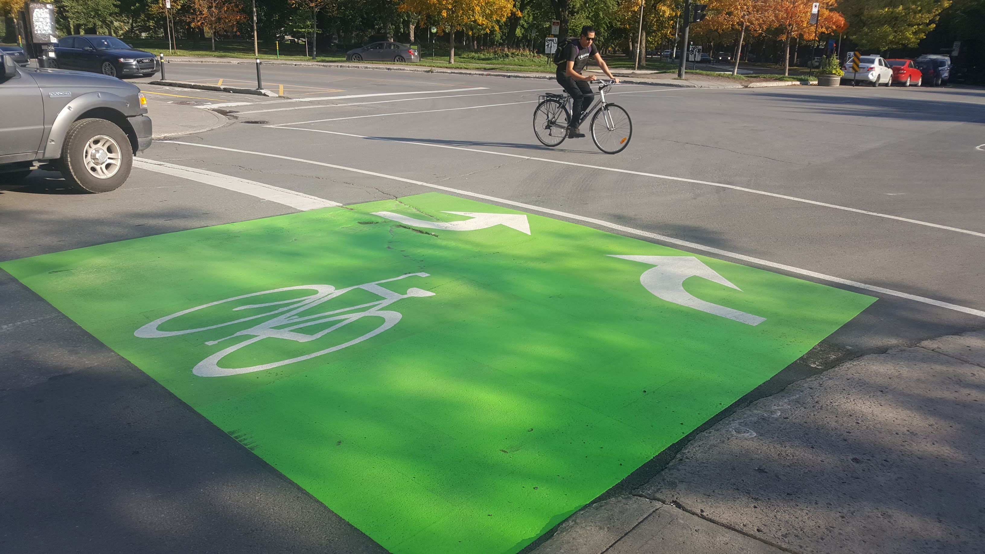 Green bike box with a white bicycle symbol and turn arrows at an intersection, a cyclist riding past