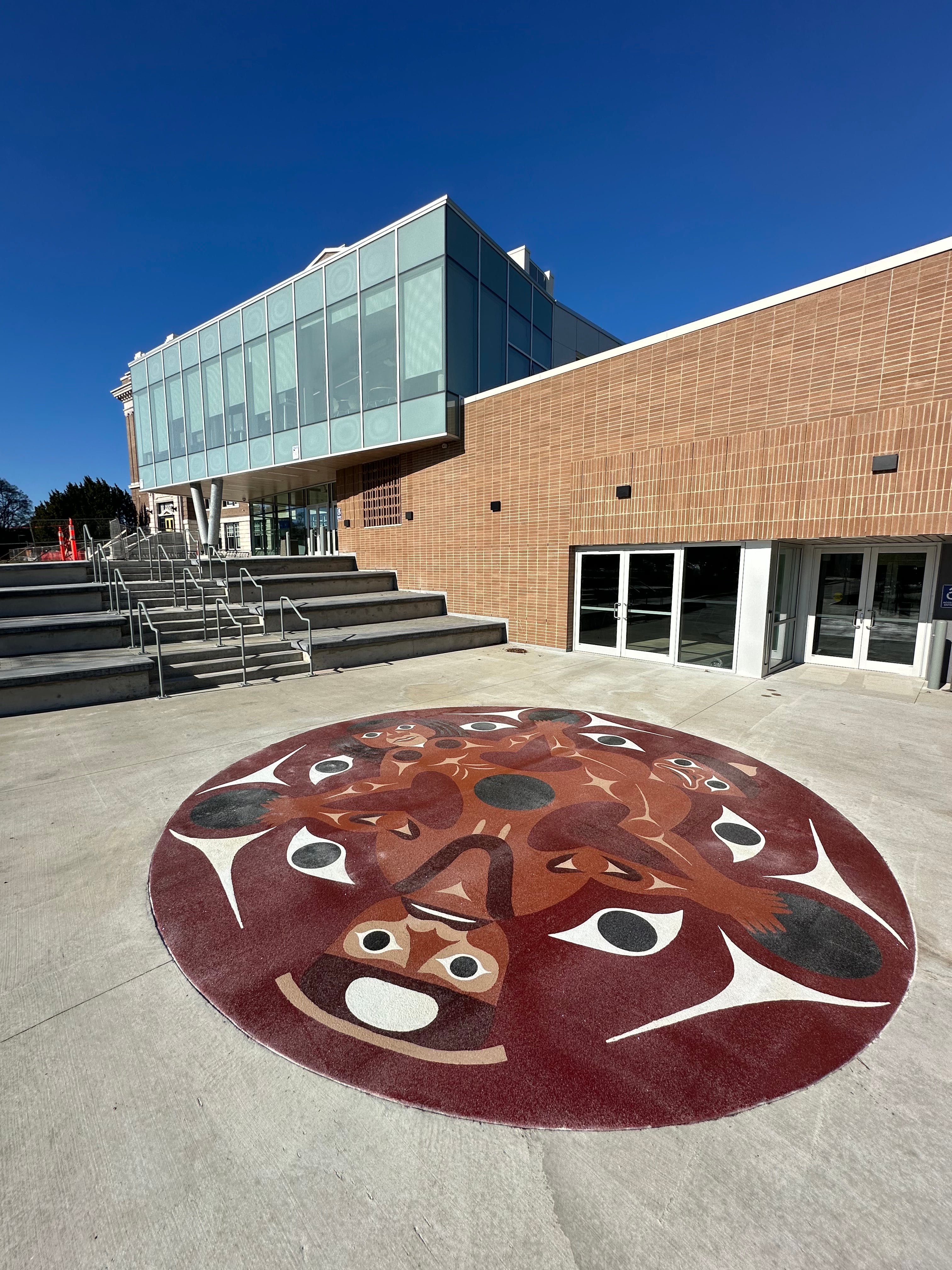 DecoMark preformed thermoplastic public art: circular Indigenous medallion artwork fused into a concrete plaza at a building entrance