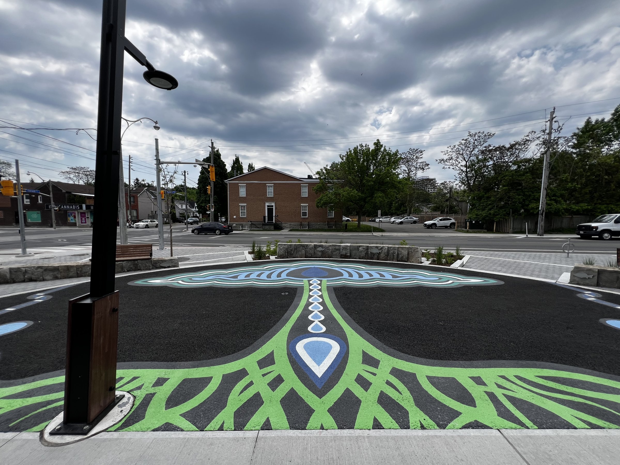 Pavement artwork of green roots and a blue water drop spreading across a street-corner plaza