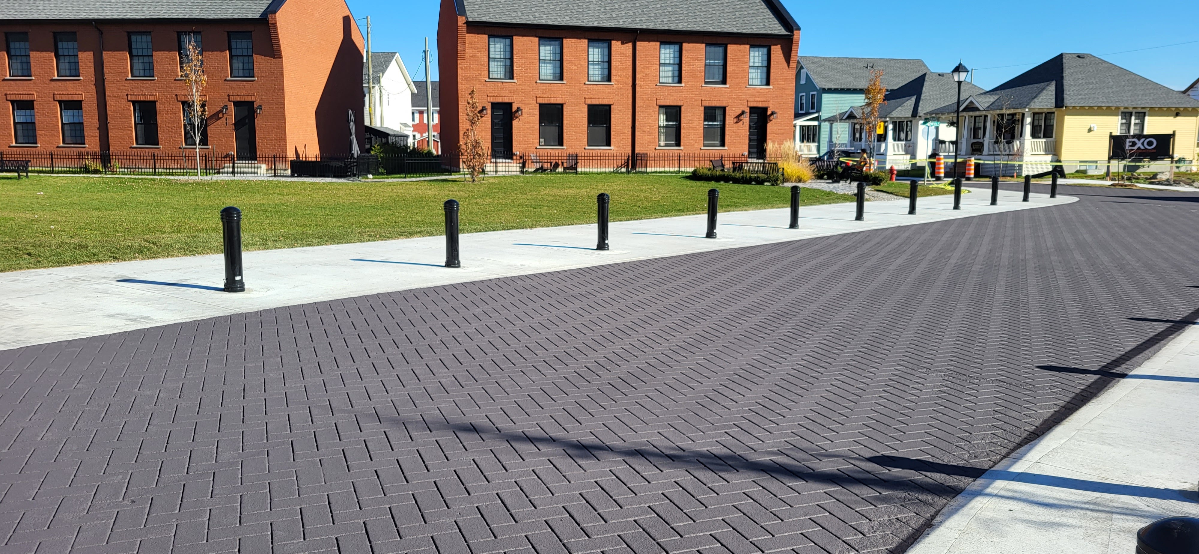 Grey StreetPrint herringbone roadway lined with black bollards in front of new brick townhomes